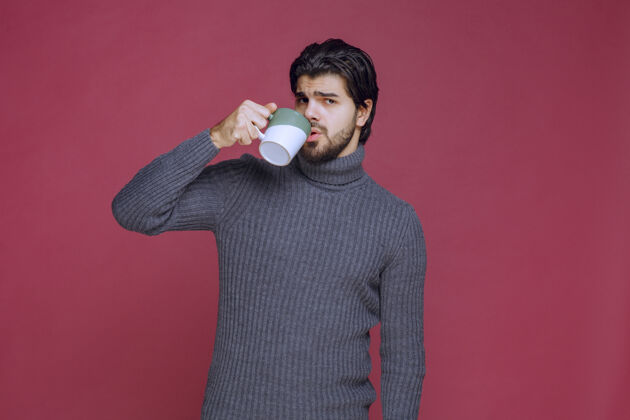 男性穿灰色毛衣的男人从杯子里喝咖啡人姿势巧克力
