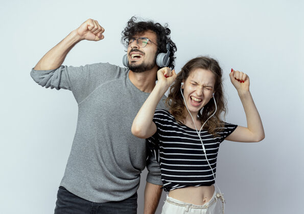 享受年轻漂亮的夫妇戴着耳机站在白色背景上欣赏音乐跳舞站立舞蹈年轻