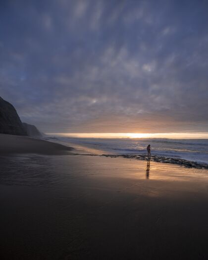 黄昏在美丽的日落中 一个小男孩走在海边的垂直镜头蓝色年轻海岸线
