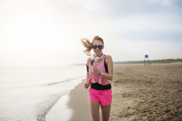 耳机特写在海边慢跑的健康年轻人移动海洋女士