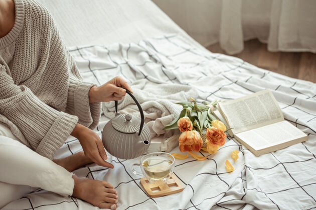 早晨一个女人在床上休息 茶 一本书和一束郁金香花舒适休息一天