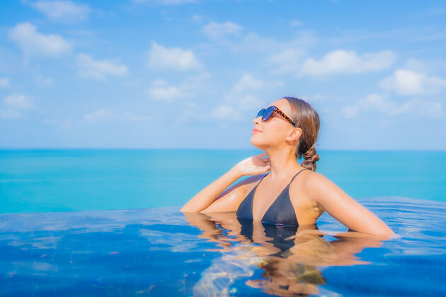 健康肖像美丽的亚洲年轻女子放松微笑休闲周围的室外游泳池在度假酒店海景中国泳装女性