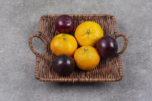 团体柳条篮子上放着新鲜的甜橘子和李子营养李子柑橘