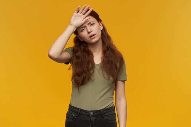 情绪疲惫的 疲惫的 长着姜黄色头发的女士的画像穿着绿色t恤人和情感概念触摸她的额头 感觉不舒服被隔离在橙色的墙上生病女孩年轻