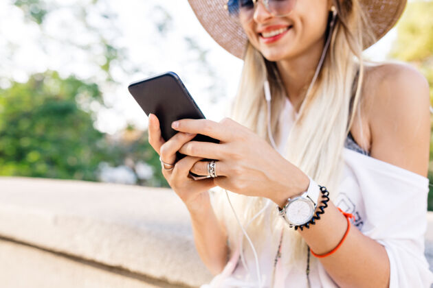 女性特写镜头：一个女孩拿着手机和耳机 一边听音乐 一边微笑漂亮的女孩拿着手机 带着巨大的情感发送信息在线智能年轻