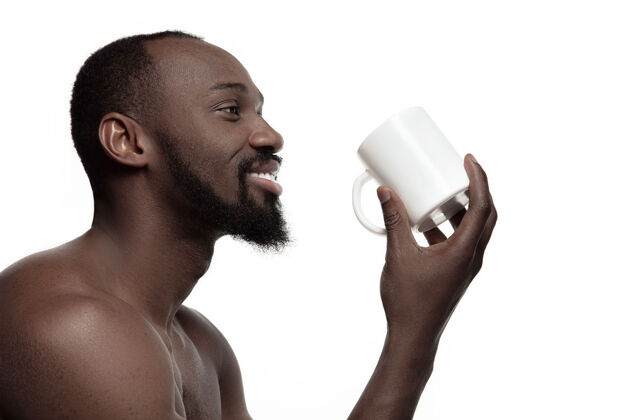 杯子一个喝着白茶或咖啡的非洲男人 被隔离在白色的工作室背景上一个年轻的裸体快乐的非洲男人的极简风格的特写肖像男孩喝酒白