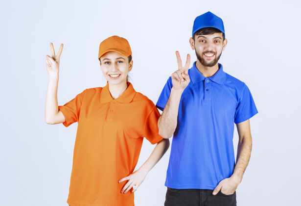 雇员身着蓝黄制服的男女快递员 展示着快乐和幸福的标志阳刚女人强壮