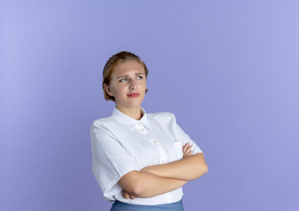 俄国人年轻恼怒的俄罗斯金发女孩交叉双臂看着侧面 紫色背景上有空白侧线恼怒年轻