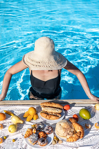 顶视图一个女孩站在清澈湛蓝的池水里 吃着美味的早餐度假村热牛角包