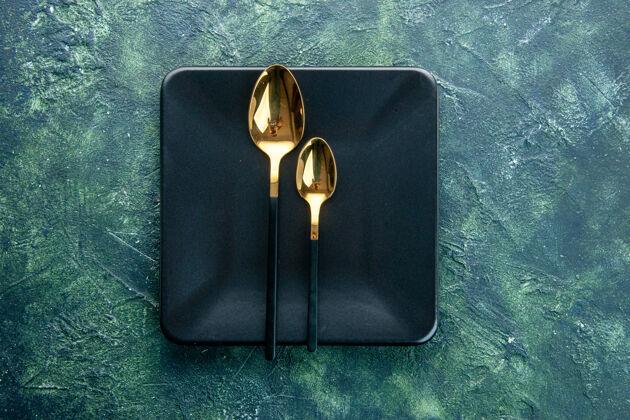 黑色方盘子俯视图黑色方形盘子 深蓝色背景上有金色勺子晚餐餐厅餐具颜色餐盘设备晚餐顶部