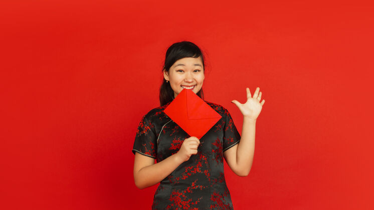服装2020年中国新年红色背景上孤立的亚洲少女肖像身着传统服装的女模特看起来很开心 微笑着 拿着红包庆祝 节日 情感年季节女孩