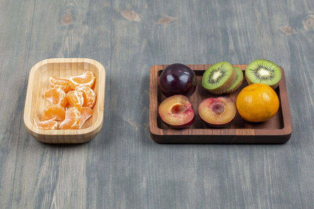 木头把新鲜的猕猴桃切成片 放在木板上 配上橘子和李子美味食物多汁