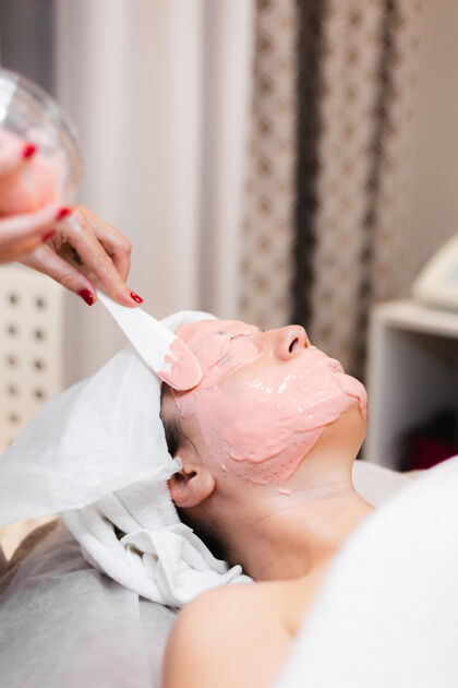 面部美容师用抹刀在女人脸上敷海藻酸钠面膜医生手谎言
