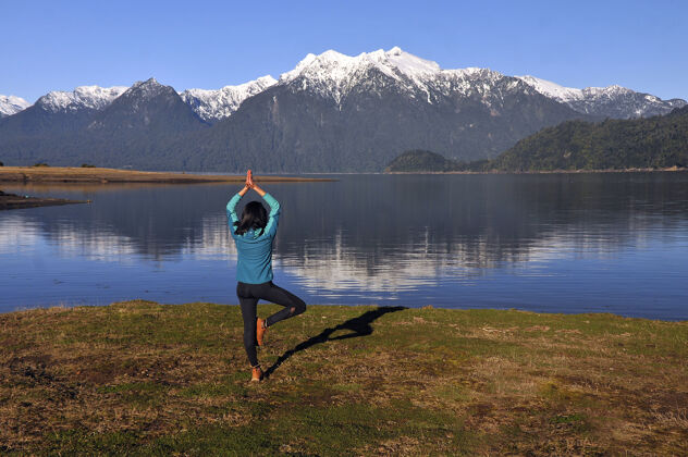 女孩穿着运动服的女人 在平静的湖光山色前摆着瑜伽姿势放松活力湖泊