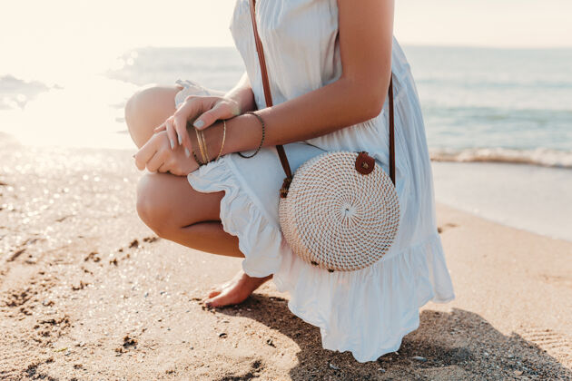 女人特写时尚细节的女人在白色连衣裙与草包夏季风格的海滩配件自然优雅稻草