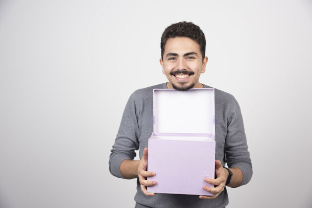 男孩带着微笑的男人 在白色的墙上放着一个打开的紫色盒子模特紫色人