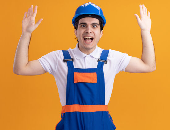 建筑年轻的建筑工人穿着建筑制服 戴着安全帽 站在橘色的墙上 惊讶地抬起手掌望着前面安全手掌男人