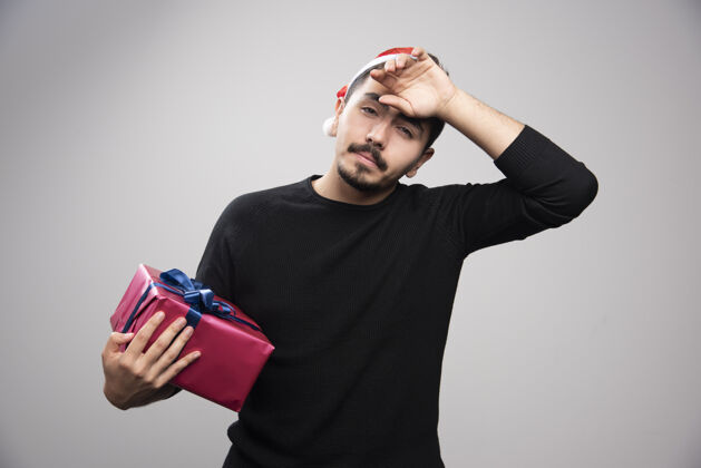 圣诞老人一个年轻人拿着一个礼品盒在灰色的墙上帽子礼物男人