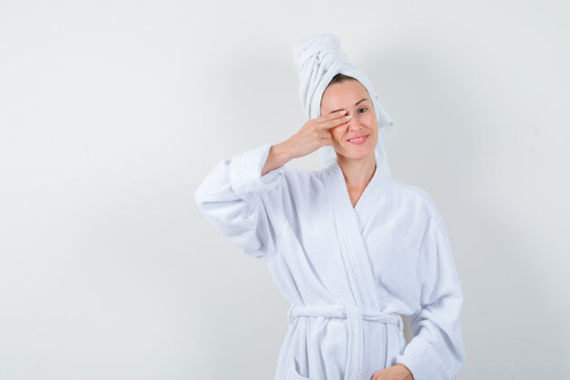 时尚照片中的年轻女子穿着白色浴衣 毛巾 手指放在眼睛上 看上去很愉快一起快乐欢呼