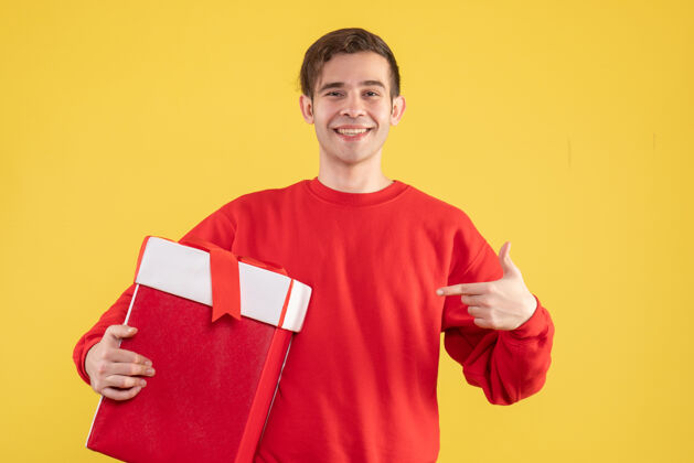 毛衣正面图穿着红色毛衣的年轻人指着黄色背景上的礼物视图年轻人指点