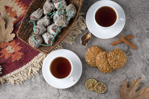 食品石头桌上放着白杯热茶 干果和燕麦片饼干营养可口小吃