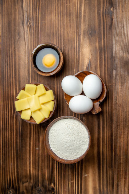 生的俯视整个生鸡蛋与面粉和奶酪在棕色桌子上鸡蛋早餐面团面团面粉粉粉顶部颜色竹子