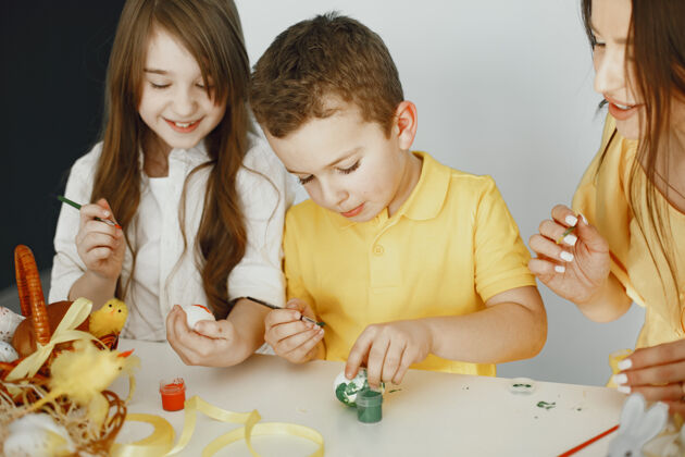 家庭孩子们画鸡蛋妈妈教孩子们坐在一张白色的桌子旁小微笑黄色