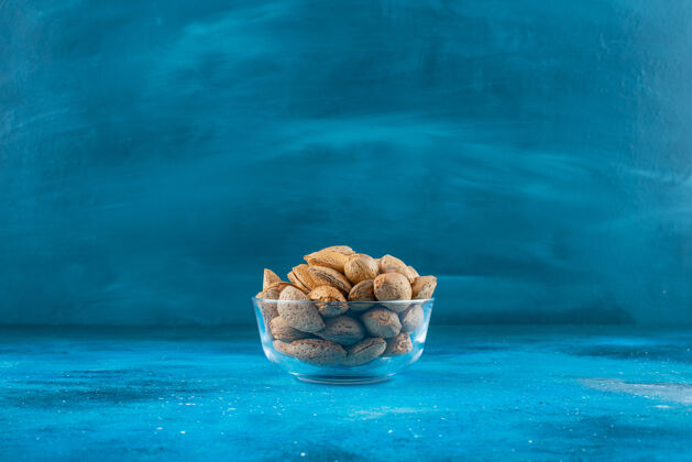 玻璃碗蓝色表面上放着一碗带壳杏仁蛋白质坚果杏仁