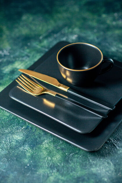晚餐正面是深色的方形盘子 背景是金色的叉刀和杯子金色深色餐具