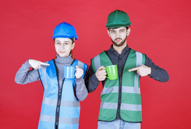 人男女工程师戴着头盔 拿着蓝色和绿色的杯子人杯子休息