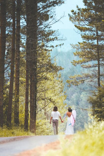 女性森林里一对新婚夫妇手举冲浪板的垂直镜头垂直婚礼松树