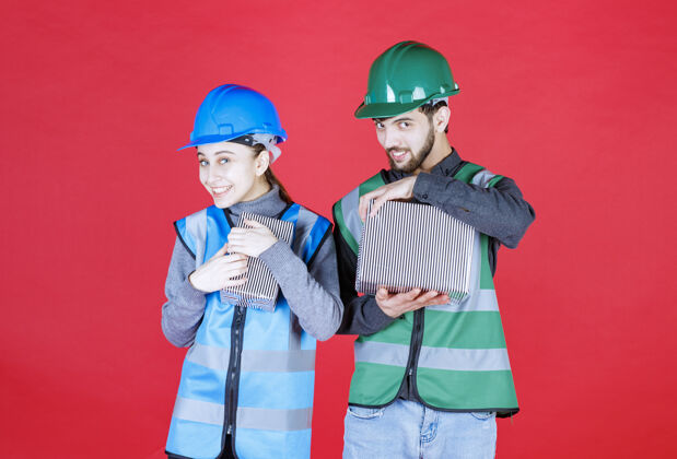 人男 女工程师戴着头盔手持银色礼盒 心情积极 面带微笑员工快乐工人