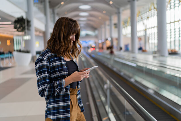 在线女性用智能手机穿过机场现代包电话