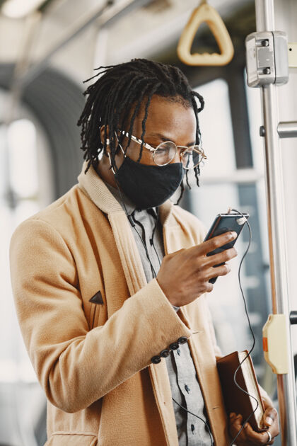 年轻人非裔美国人坐在城市巴士上穿棕色外套的家伙电晕病毒概念通勤面具公共汽车