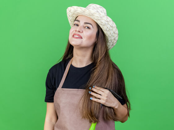 穿微笑美丽的园丁女孩穿着制服戴着园艺帽手持锄头耙孤立在绿色背景锄头帽子制服