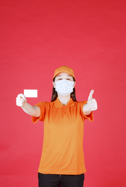 快乐身着橙色制服 戴着口罩的女服务人员出示名片并显示积极的手势成人姿势动力