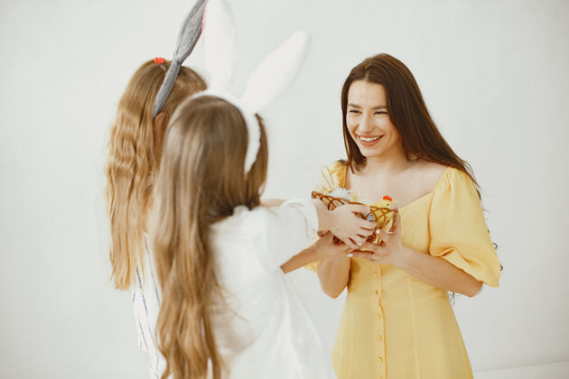家庭女孩们拿着一篮子鸡蛋快乐的妈妈穿着黄色的裙子女孩们留着长长的头发颜色室内复活节