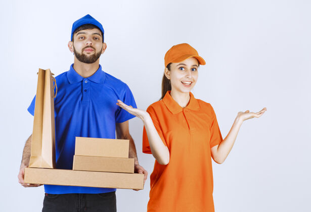 时尚穿着蓝黄制服的男女快递员手里拿着纸板外卖盒和购物包呆在家里姿势发货
