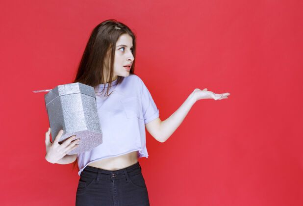 年轻人年轻女子拿着一个银色的礼盒 指着某人女士孤立介绍