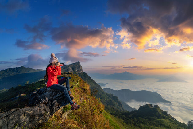 徒步旅行坐在岩石上拿着相机的旅行者在泰国清莱的doiphamon山拍照自然旅游雾