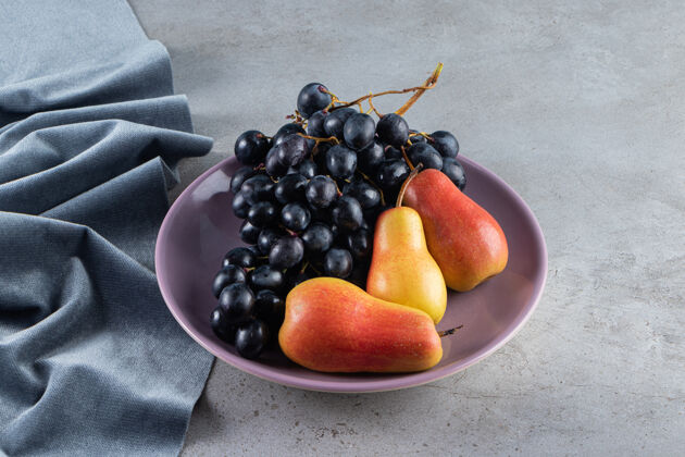 串石桌上放着一串紫盘子里的红黄梨和葡萄有机食物葡萄