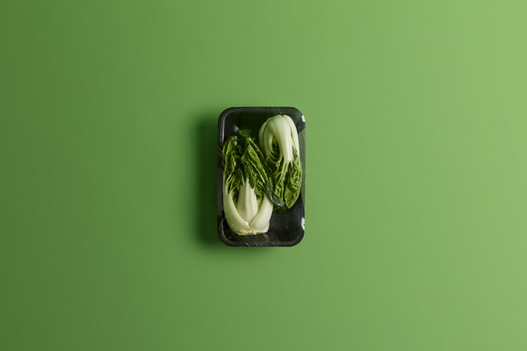 美食黑色托盘上用保鲜膜包裹的白菜或白菜绿色背景下超市出售的新鲜蔬菜健康的生活方式 茶点和营养理念生的膳食新鲜