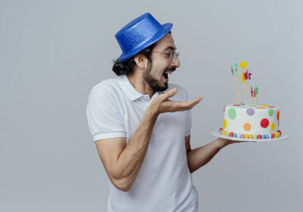 帽子快乐的帅哥戴着眼镜 戴着蓝色的帽子 手拿蛋糕指着白色的背景拿着高兴手