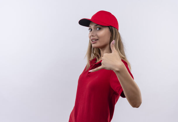 制服看着镜头 穿着红色制服 戴着帽子 在白色背景上显示出孤立的打电话手势的年轻送货女孩高兴极了女孩送货表演