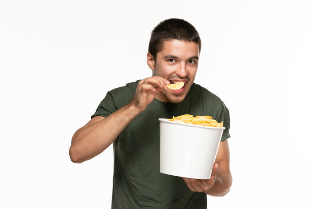 篮子正面图身穿绿色t恤的年轻男子拿着一个篮子 里面放着土豆 在白墙上吃着 孤独地享受着电影杯子电影院电影