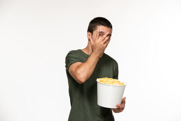电影院正面图身穿绿色t恤的年轻男性手持土豆cips在白色办公桌上看电影孤独的人咖啡电影杯子