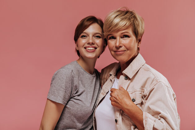 衬衫漂亮的两个现代短发女人 穿着时髦的衣服 微笑着 拥抱着 看着粉色背景下的镜头女士夹克成人