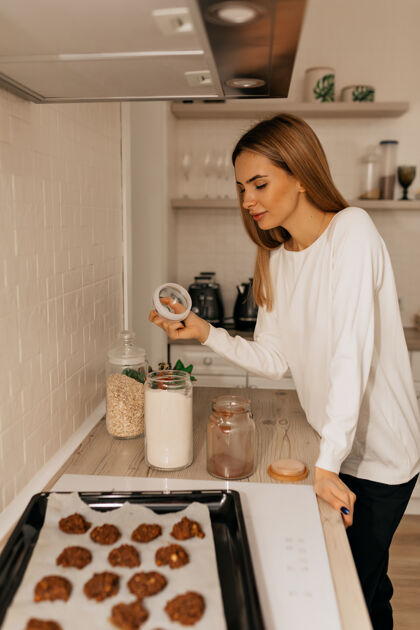 积极可爱的年轻女士站在厨房里做饼干快乐的女人站在家里厨房里装饰自制的纸杯蛋糕工作女士平衡