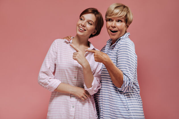 老年人快乐的两位女士 短发 粉色和蓝色条纹夏装 微笑着 展示着在孤立的背景上放置文字成人白色女士
