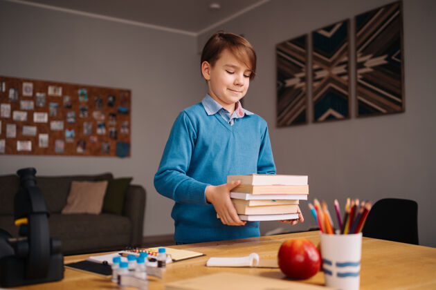 小学一年级男生在家学习 手里拿着一堆书 准备上网上课隔离家庭学校学习